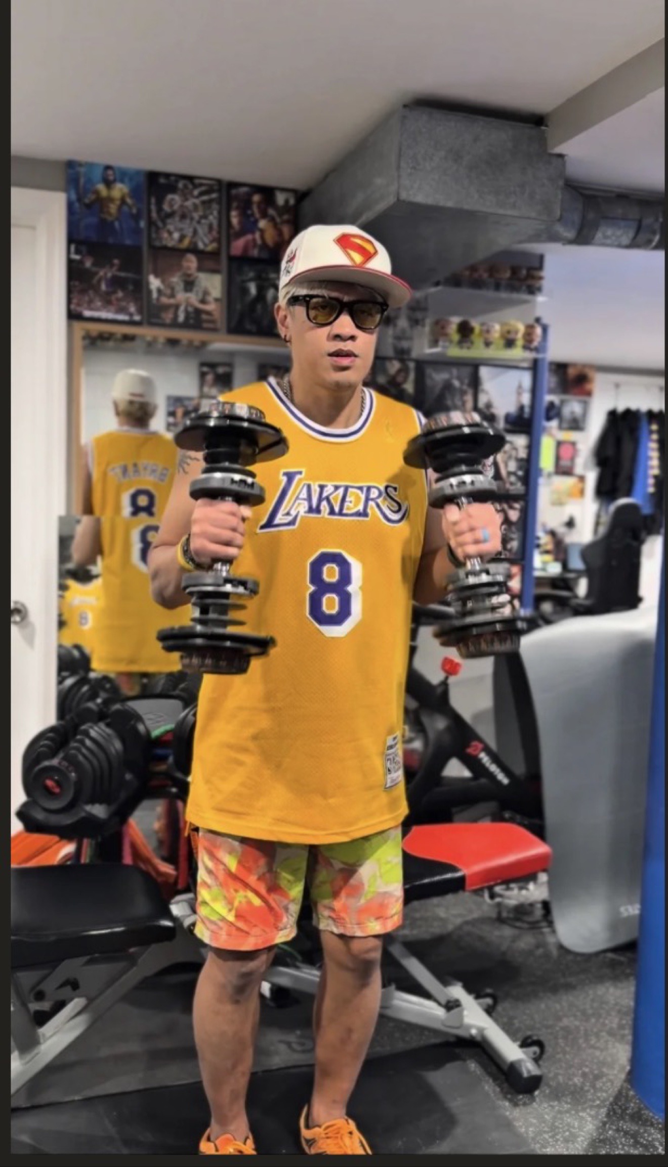 Coach Mike in a Lakers number 8 jersey and Superman cap holding dumbbells at Wolf's Den