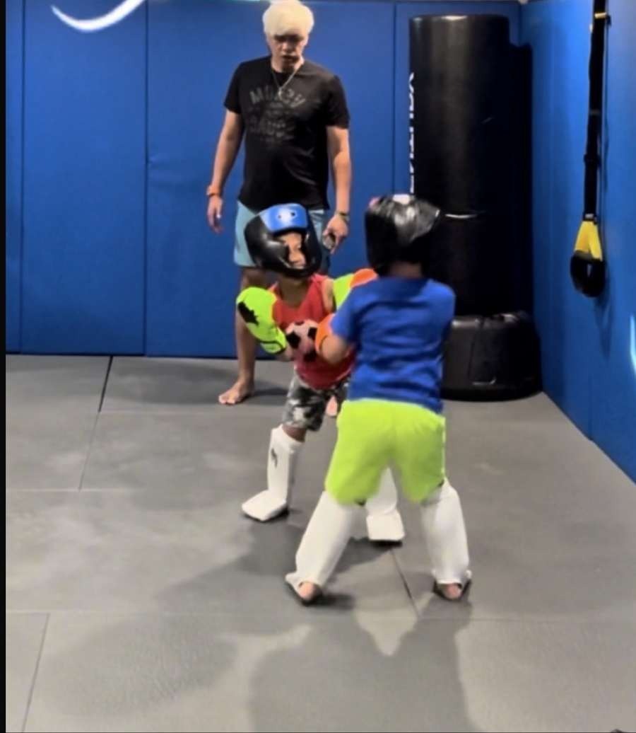 Two kids sparring with headgear while Coach Mike watches at Wolf's Den