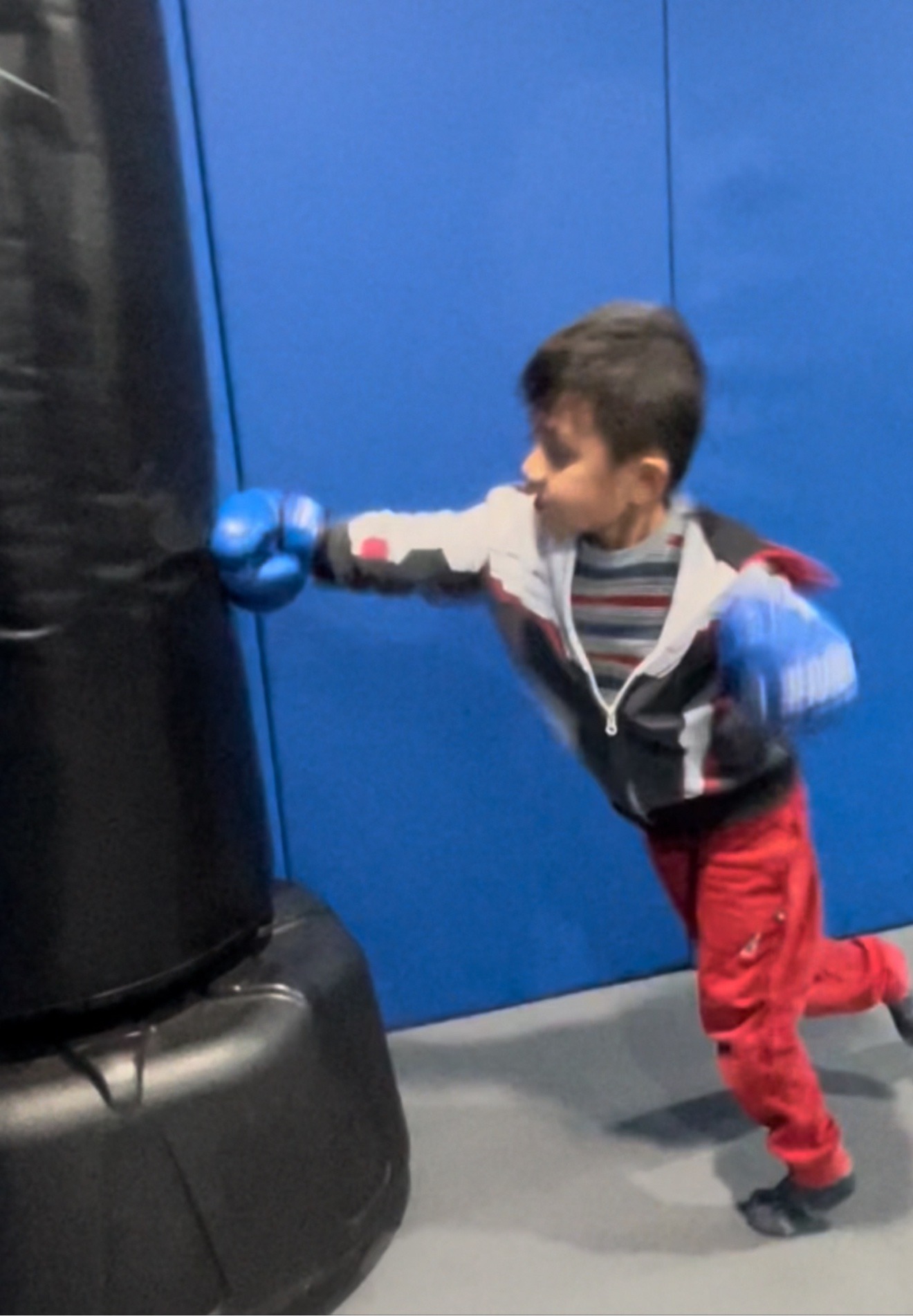 Young boxer in blue gloves practicing punches on a heavy bag